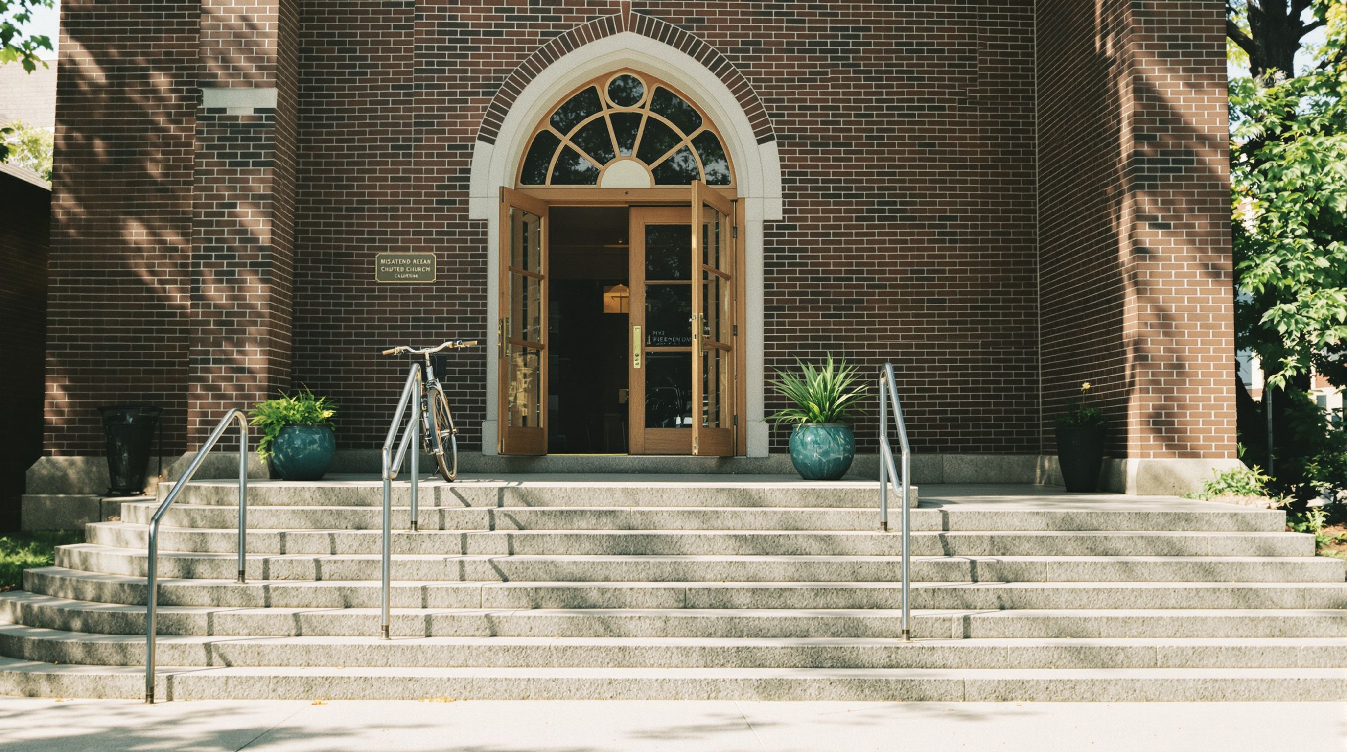 Stone steps leading to the open wooden doors of a small brick church on a sunny morning